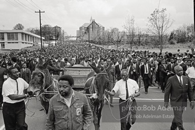 Free at last: King goes to his rest,  Atlanta, Georgia.   1968-


“With more than 50,000 mourners from all over the world following, King’s earthly remains were borne on a simple country wagon pulled by two mules. It was fitting: A wooden wagon was basic transport for the disadvantaged and disinherited, the people he served in his very public ministry. King’s life was dedicated to service. He studied, strategized, exhorted, prayed, marched, pleaded, protested, negotiated and spoke, all to remedy long-standing injustices. “In his Gehenna he suffered vilification, numerous jailings, ’round-the-clock telephone threats, stonings, several bombings, a stabbing, repeated beatings, cross burnings, nervous exhaustion and, finally, an assassin’s bullet. King died serving the dispossessed, and they understood this and adored him for it. Country people would and did drop to their knees as he passed, bawling out,     ‘de Lawd!’”