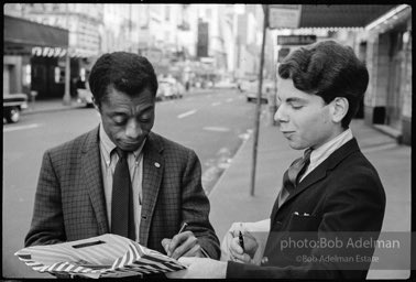 Outside the ANTA Washington Square Theater, James Baldwin signs his autograph for a young fan. New York City, 1964.
