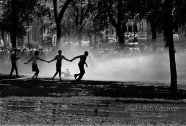 Demonstrators hold on to one another to face the spray, Kelly Ingram Park,  Birmingham,  Alabama.  1963

“The force of the spray from the fire hose was so powerful that it peeled the bark off the trees. Protestors skidded along the grass, propelled by the torrent.”